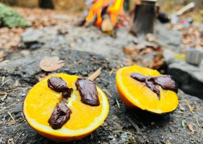 Die Schokolade ist geschmolzen, die Schoggi-Orangen sind bereit zur Verkostung. Im Hintergrund ist ein brennendes Feuer und eine Kaffeekanne zu sehen.