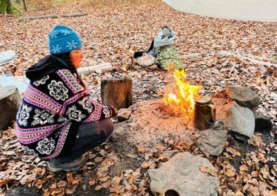 Lorenza Marconi schaut verträumt in ein friedlich brennendes Feuer. Neben ihr steht eine Teekanne und eine samische Holztasse (Samen = in Lappland lebendes Urvolk).