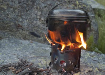 Ein Feuertopf auf einem Hobo-Kocher, eine faltbare Metallbox um ein kleines aber sehr effizientes Kochfeuer zu entzünden, inspiriert vom Dosenfeuer der Nord Amerikanischen Hobos (Hobo = Obdachloser).